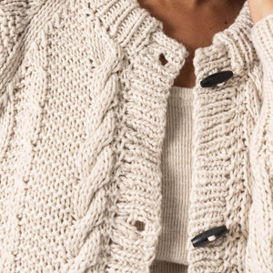 Close-up of a person wearing a beige knitted cardigan with button details.