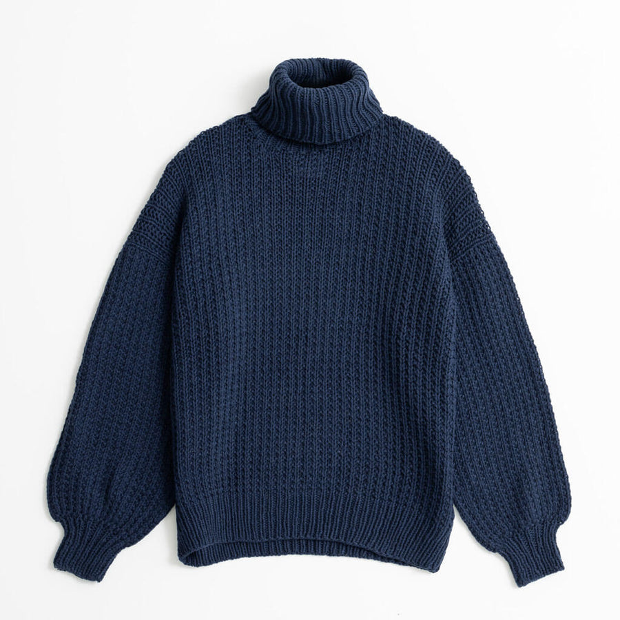 Woman wearing a dark blue turtleneck sweater sitting on a chair against a white background