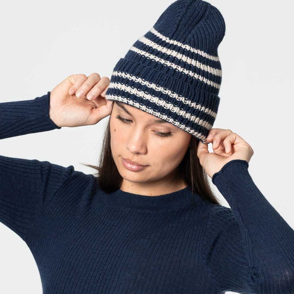 Woman wearing a navy blue and white striped beanie against a light gray background