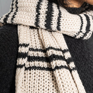 Close-up of a person wearing a white knitted scarf with black stripes.