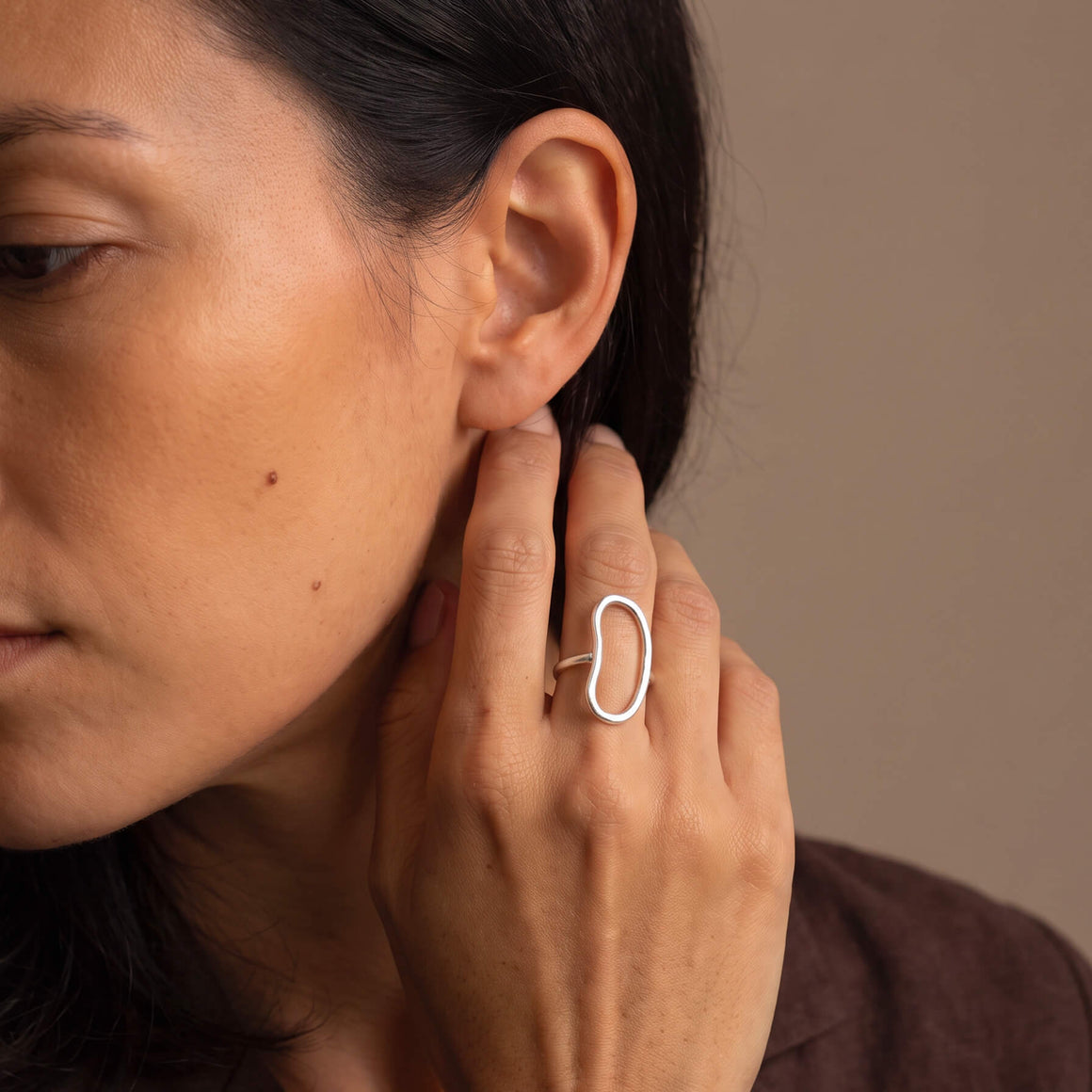 A close-up lifestyle shot of a woman wearing a minimalist, open oval-shaped silver ring on her finger.