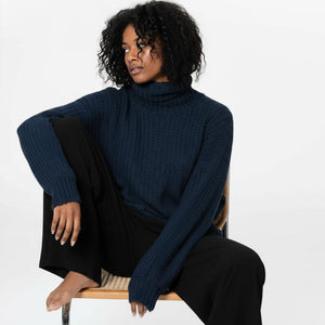 Woman wearing a dark blue turtleneck sweater sitting on a chair against a white background