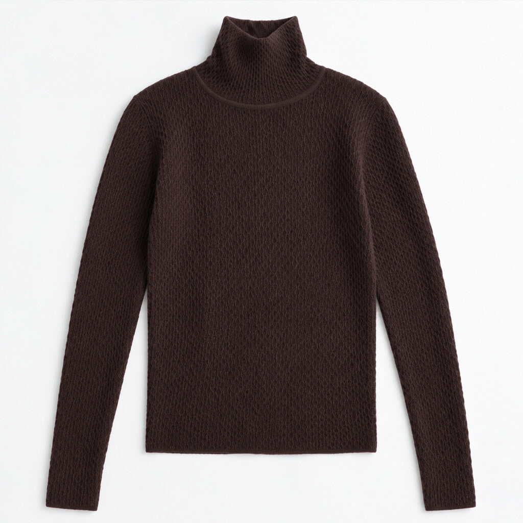 A woman with long dark hair is shown from the side in a studio setting, wearing a fitted ribbed turtleneck sweater in dark brown with light blue jeans against a solid tan background.