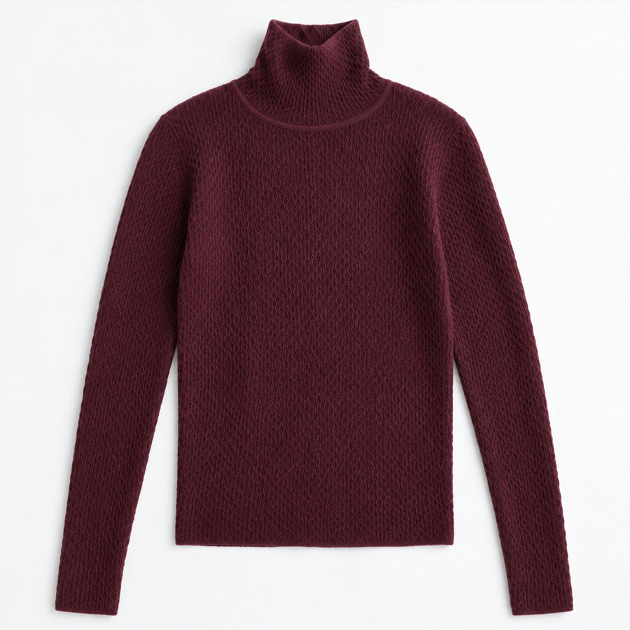 A woman wearing a dark burgundy ribbed turtleneck sweater and black skirt, posing against a solid beige studio background.