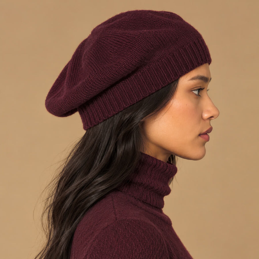A woman wearing a deep burgundy knit beret and matching ribbed turtleneck sweater against a solid beige background.