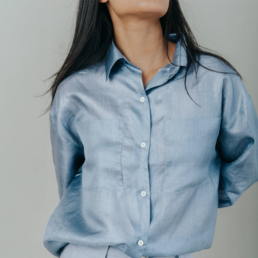 A woman modeling a light blue long-sleeve button-up shirt with a high collar, photographed against a plain light gray studio background.