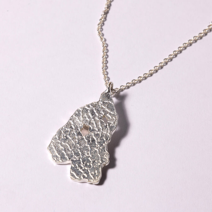 Close-up of a woman wearing a silver necklace with a pendant against a dark background