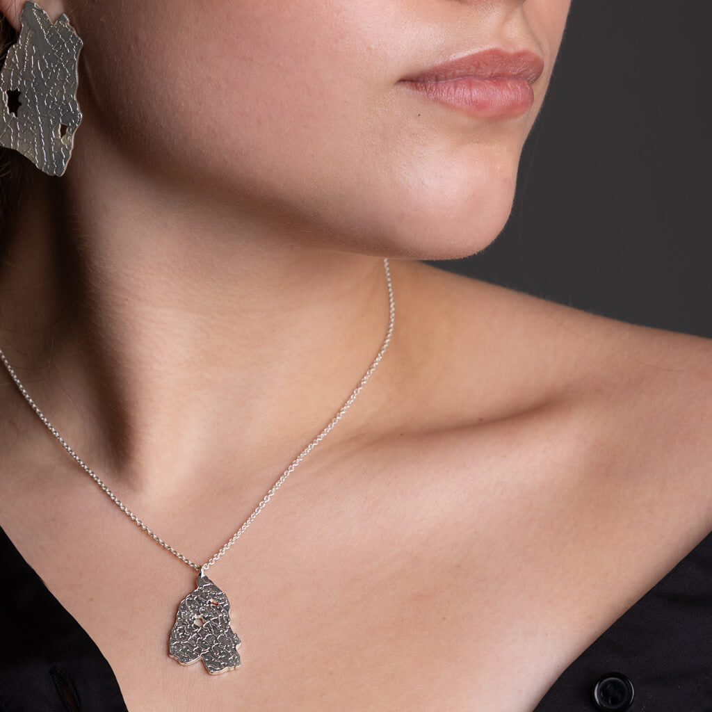 Close-up of a woman wearing a silver necklace with a pendant against a dark background